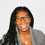 A vibrant portrait of a smiling woman with dreadlocks and glasses, exuding joy.