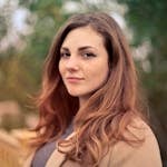 A young woman with long hair smiles confidently for an outdoor portrait session.